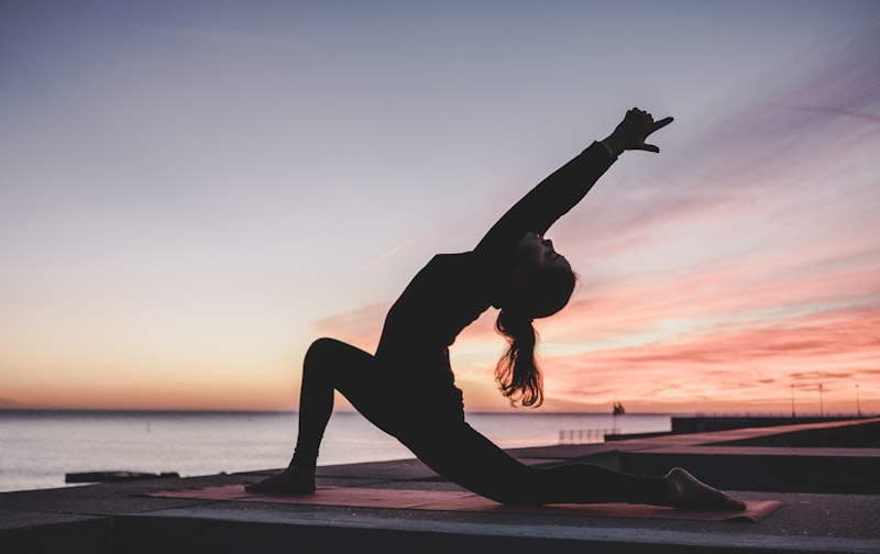 Silhouette of a person in a yoga stretch by the water at sunset during a quiet wellness break